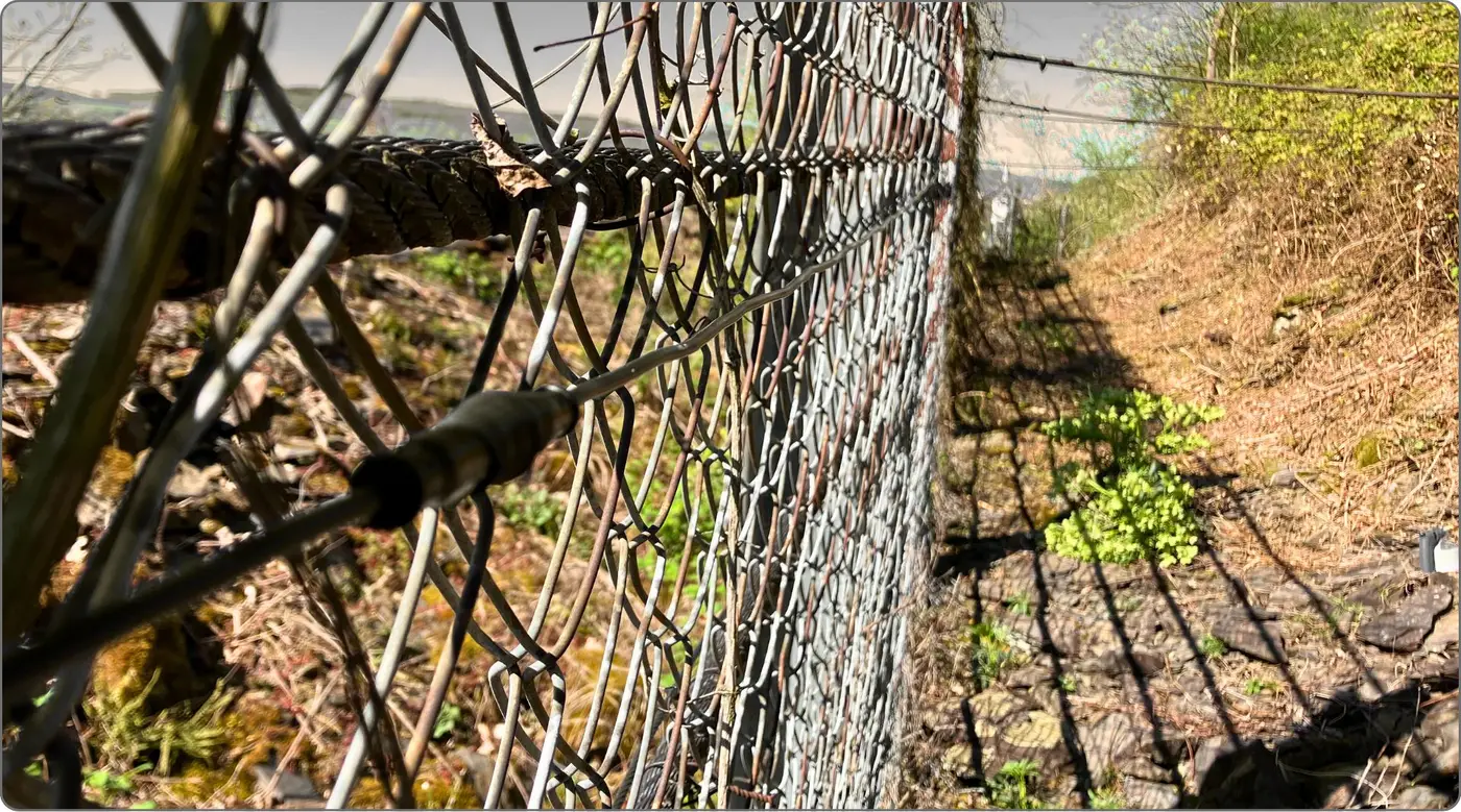 Wire mesh of a slope stabilisation with sensor cable, embankment in the background