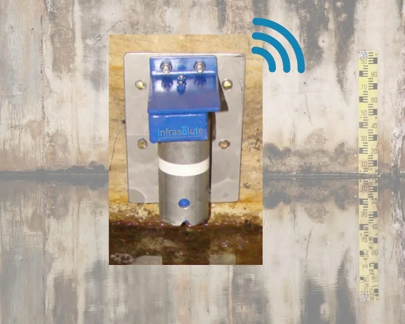 Pegelsensor an einer Betonwand über der Wasseroberfläche, daneben eine Messlatte