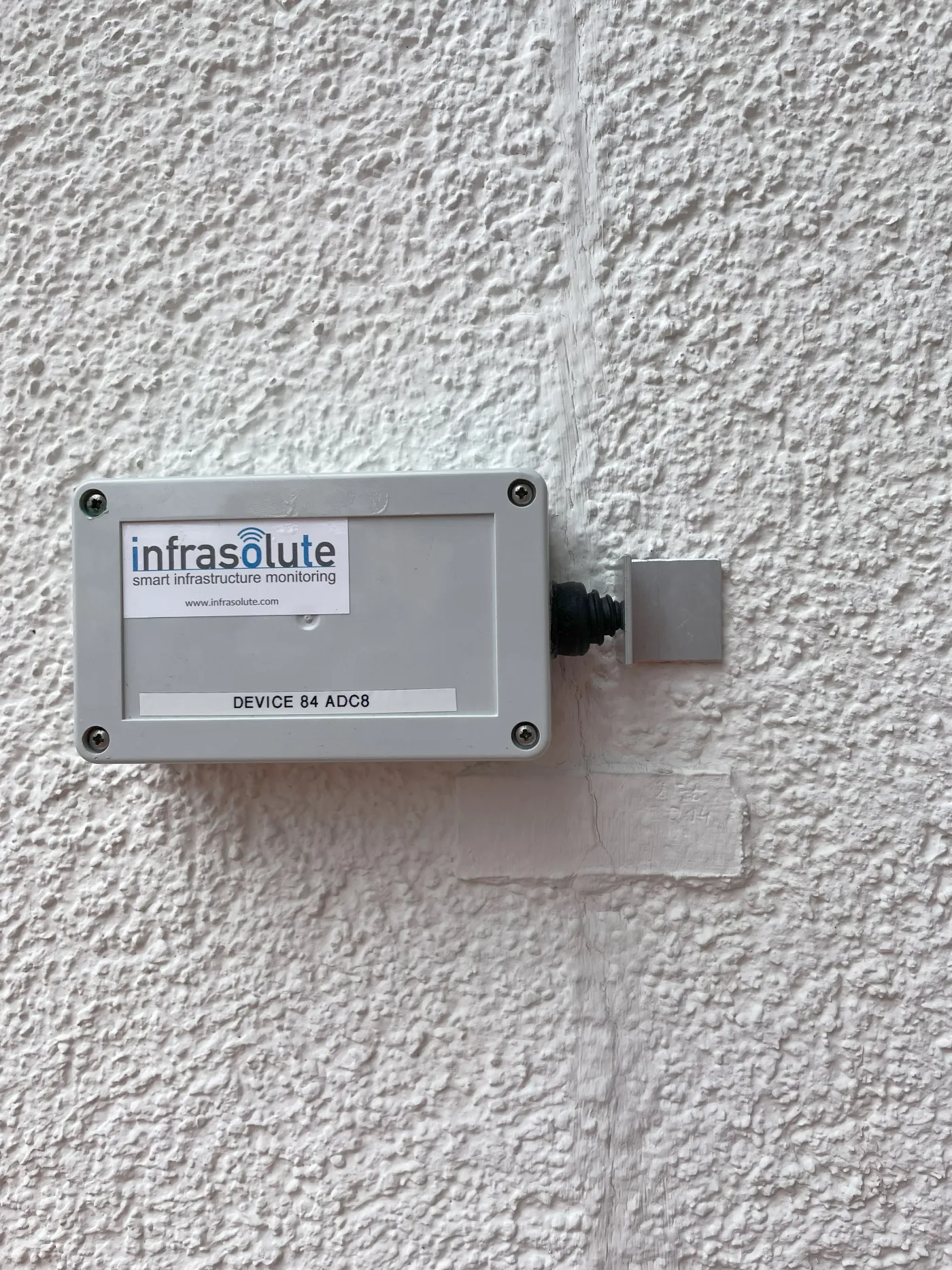Crack sensor mounted on a plastered facade above a crack, with a displacement transducer on the opposite side