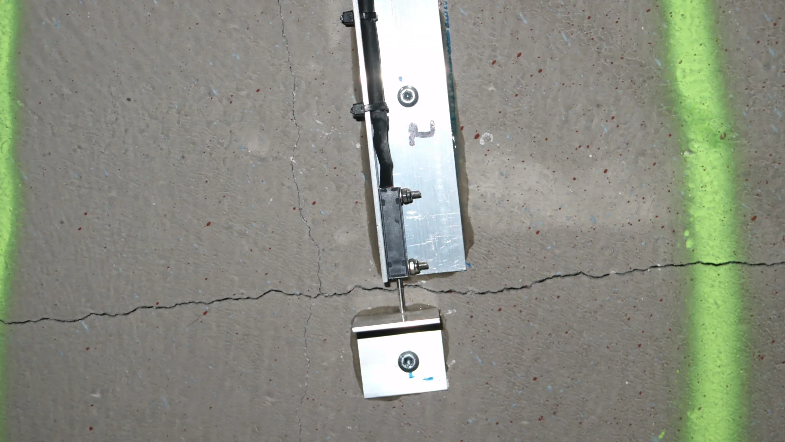 Displacement transducer of the crack sensor over a crack in a concrete wall, with a bracket on both sides of the crack