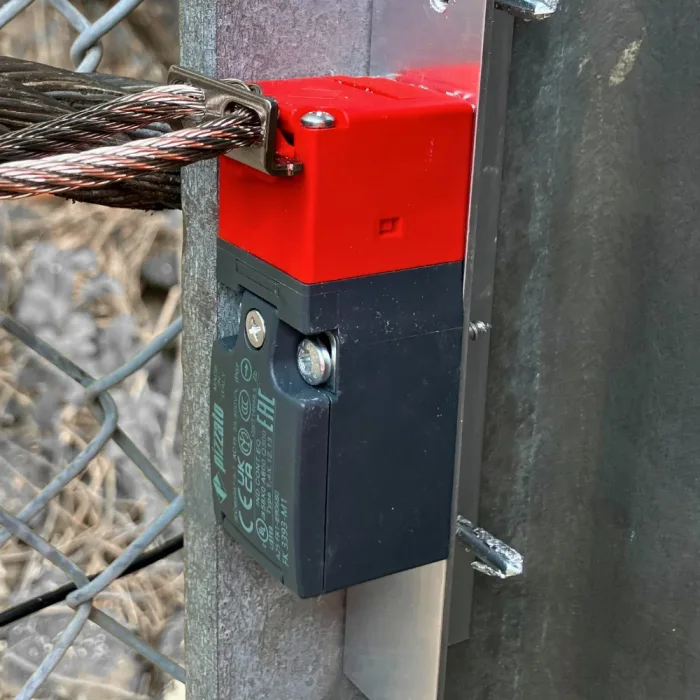 Seilzugsensor am Zaunpfosten, mit dem Drahtseil der Auffangbarriere verbunden